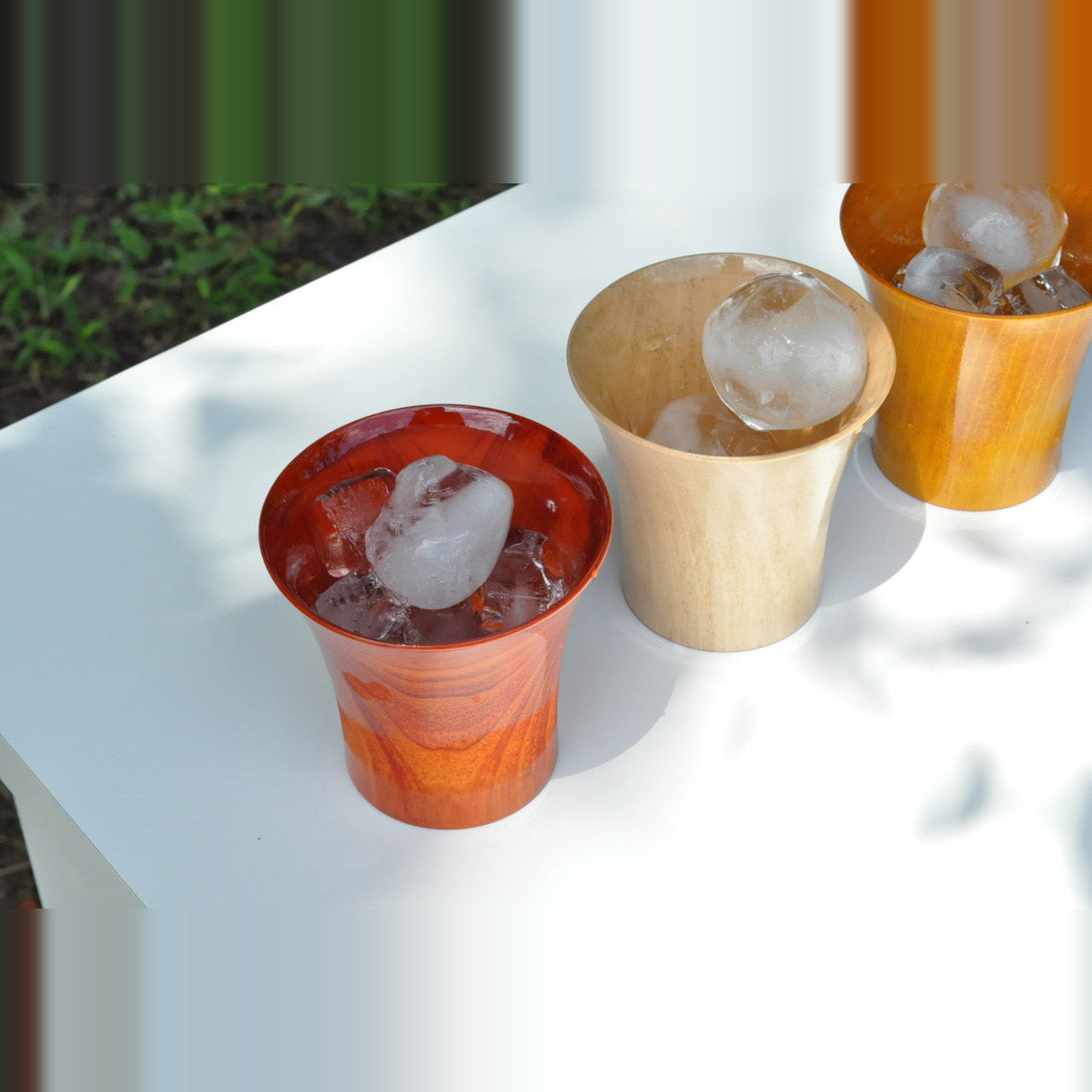 山中漆器のロックカップ クールカップ―屋外の卓に赤・生成り・黄の3客。丸い氷が溶けずに残っている
